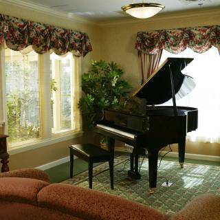 A grand piano in a cozy living room with large windows and elegant decor.