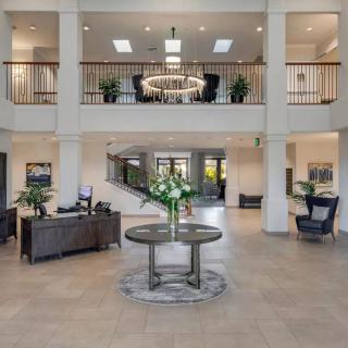 A spacious and elegantly designed lobby featuring modern furniture, a central table with flowers, and a grand chandelier.