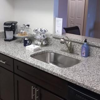 A kitchen with a granite countertop featuring a sink, coffee maker, and soap dispenser.