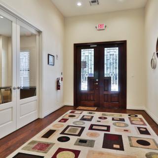 A well-lit entrance hallway featuring a patterned area rug and double glass doors.