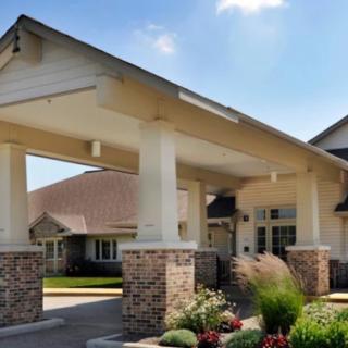 The image shows the entrance of a modern building with a covered walkway and landscaped surroundings.