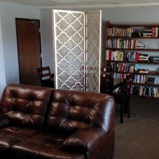 A cozy living room featuring a brown sofa, bookshelves filled with books, and a decorative partition.