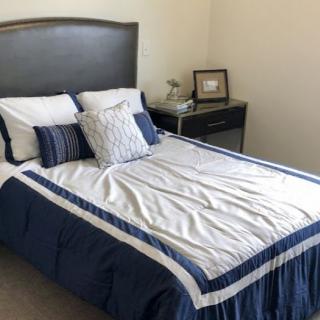 A neatly arranged bedroom featuring a bed with white and blue bedding, accompanied by pillows and a nearby nightstand.