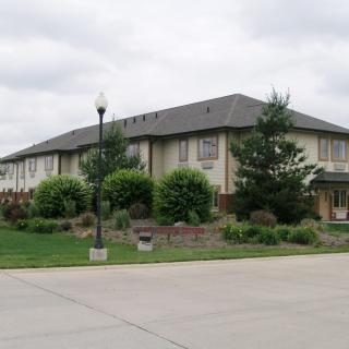 A suburban residential building surrounded by greenery under a cloudy sky.