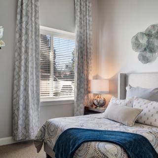 A cozy bedroom with a decorative bed, window with curtains, and a bedside lamp.