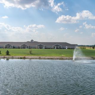 A scenic view of a building alongside a tranquil pond featuring a fountain.