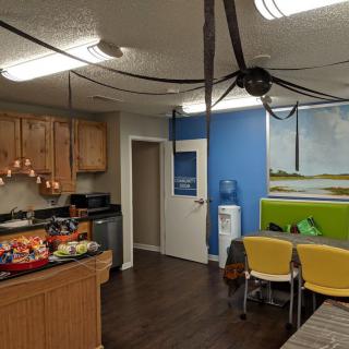 An office kitchen area decorated for Halloween with a large spider hanging from the ceiling and a bowl of candy on the counter.