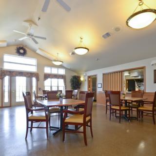 A spacious dining area with several tables and chairs, featuring ceiling fans and large windows.