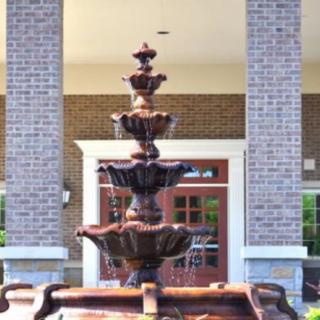 A decorative multi-tiered fountain in front of a brick building entrance.