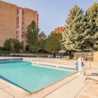 An outdoor swimming pool surrounded by trees and buildings in an apartment complex.