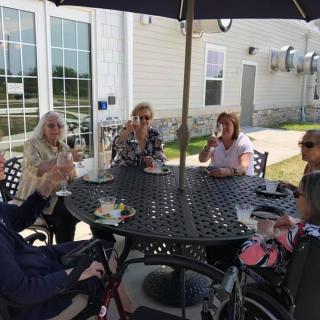 Elderly women enjoying a social gathering at an outdoor patio under a large umbrella.