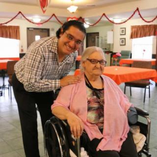 A friendly interaction in a care home setting, featuring an elderly person in a wheelchair and a companion.