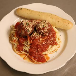 A delicious plate of spaghetti with meatballs in tomato sauce, accompanied by a breadstick.