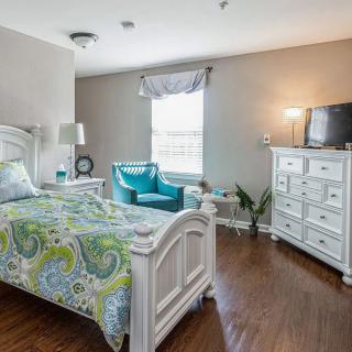 A cozy bedroom with a bed, dresser, and teal chair near the window.