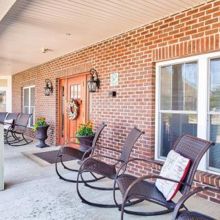A welcoming front porch with rocking chairs and decorative plants against a brick exterior.