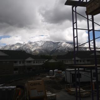 A view of snow-capped mountains under a cloudy sky, framed by construction scaffolding.