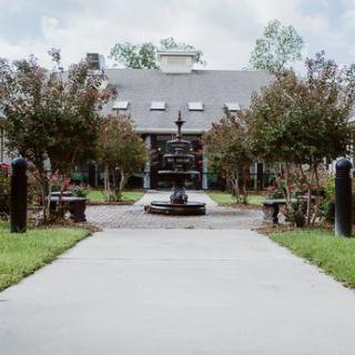 A scenic view of a pathway leading to a building with a fountain and well-maintained landscape.