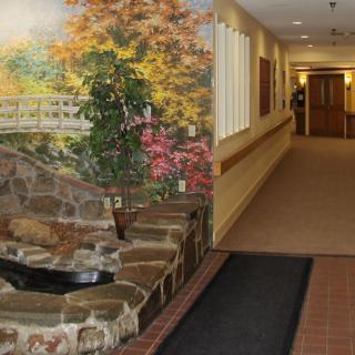 A hallway with a decorative mural featuring a nature scene, alongside a stone structure and plants.