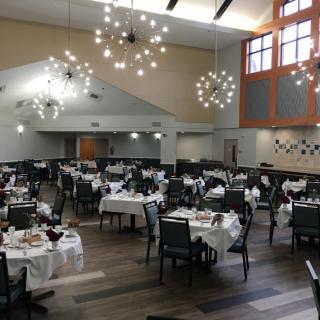 A spacious and elegantly designed dining hall with set tables and modern chandeliers.
