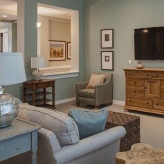 A cozy living room with a sofa, armchair, and a television mounted above a wooden dresser.
