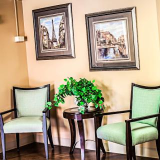 A cozy waiting area featuring green chairs, a small table with a plant, and framed artwork on the walls.
