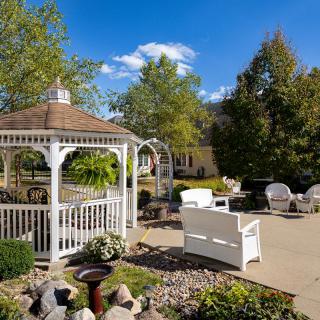 A peaceful garden setting with a white gazebo and outdoor seating area under a clear blue sky.