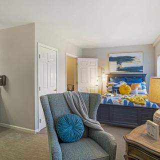 A cozy bedroom with a modern design, featuring a blue armchair, stylish bedding, and abstract artwork.