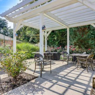 A peaceful outdoor patio with a pergola, featuring tables and chairs surrounded by a lush garden setting.
