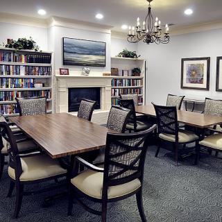 A well-organized library meeting room featuring a central table surrounded by chairs, bookshelves, a fireplace, and elegant lighting.