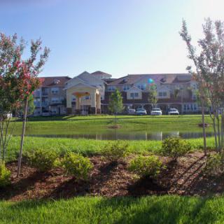 A residential building surrounded by greenery and a pond on a sunny day.