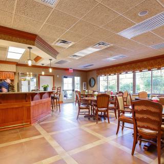 A welcoming dining area with wooden tables and chairs, filled with natural light from large windows.