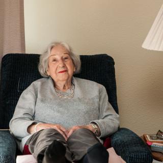 An elderly woman sitting comfortably in a living room chair.