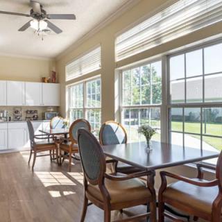 A bright dining space with large windows, featuring a table set and access to a kitchen area.