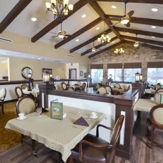 A spacious restaurant dining area featuring elegant chandeliers, wooden beams, and neatly arranged tables and chairs.