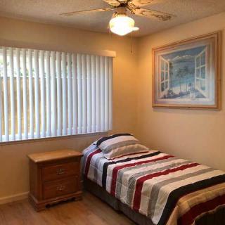 A cozy bedroom with a single bed and wooden furniture, featuring striped bedding and a ceiling fan.