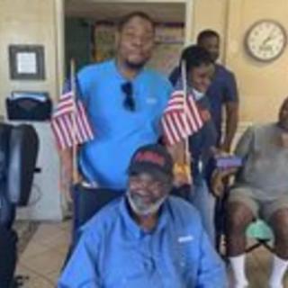 A group of people indoors, with a man in a wheelchair holding American flags.