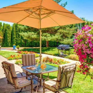A cozy patio setup with a table, chairs, and an umbrella in a sunny garden.