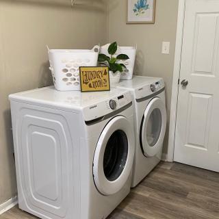 A tidy laundry room with a washing machine and dryer, decorated with a plant and a laundry basket.