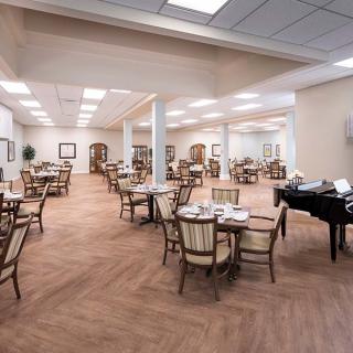 A spacious and empty dining hall with neatly arranged tables and chairs, featuring a piano in the corner.