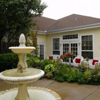 A charming patio area with a fountain, surrounded by lush greenery and outdoor seating.
