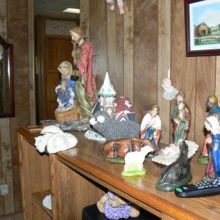 A display of religious figurines and nativity scenes on a wooden shelf, set against wood-paneled walls.