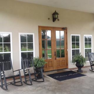 A welcoming front porch with wooden double doors, rocking chairs, and potted plants.