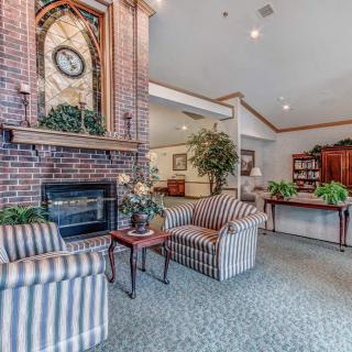 A cozy living room with a brick fireplace, striped chairs, and traditional decor.