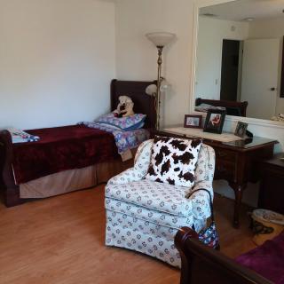 A cozy bedroom with a bed, armchair, and a floor lamp near a mirror.