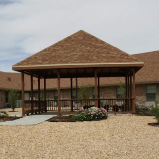 A wooden pavilion situated in a landscaped area with gravel and flowering plants.