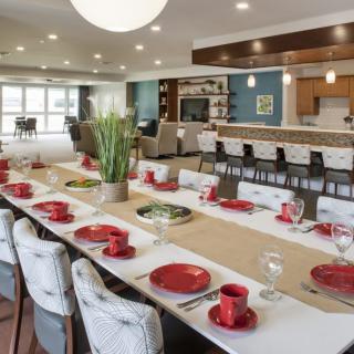 A modern dining room with a stylish table setting featuring red dishes and an open layout leading to a kitchen bar.