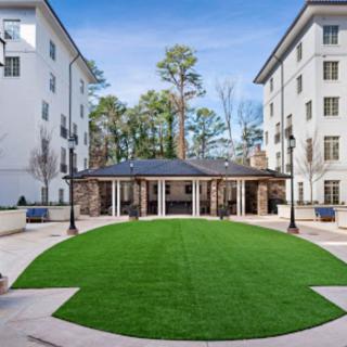 A neatly landscaped courtyard surrounded by buildings with a central grassy area and trees in the background.