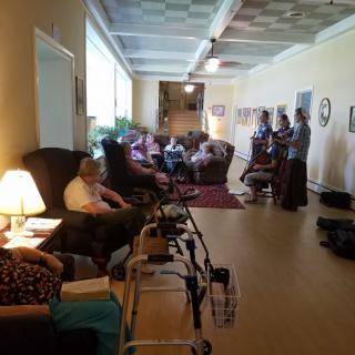 A relaxing common area in a nursing home with several elderly people seated and a walker nearby.