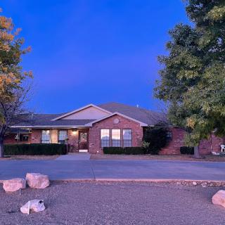 A brick house surrounded by trees during the evening, with a spacious driveway in front.