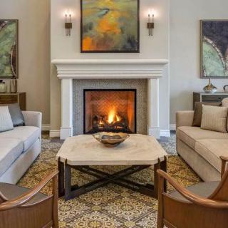 A cozy living room featuring a central fireplace, surrounded by sofas and chairs, with artwork adorning the walls.